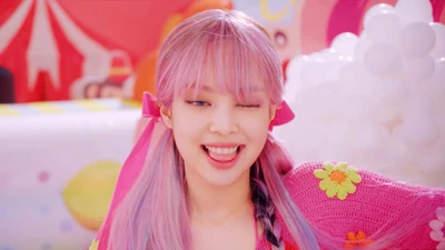 Jennie von BLACKPINK zwinkert verspielt und lächelt, während sie ihre pinken Haare und ihr buntes Outfit in einer lebhaften, zuckerhaltigen Umgebung präsentiert.