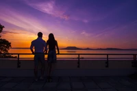 Silhueta de um casal olhando para um vibrante pôr do sol sobre um lago tranquilo