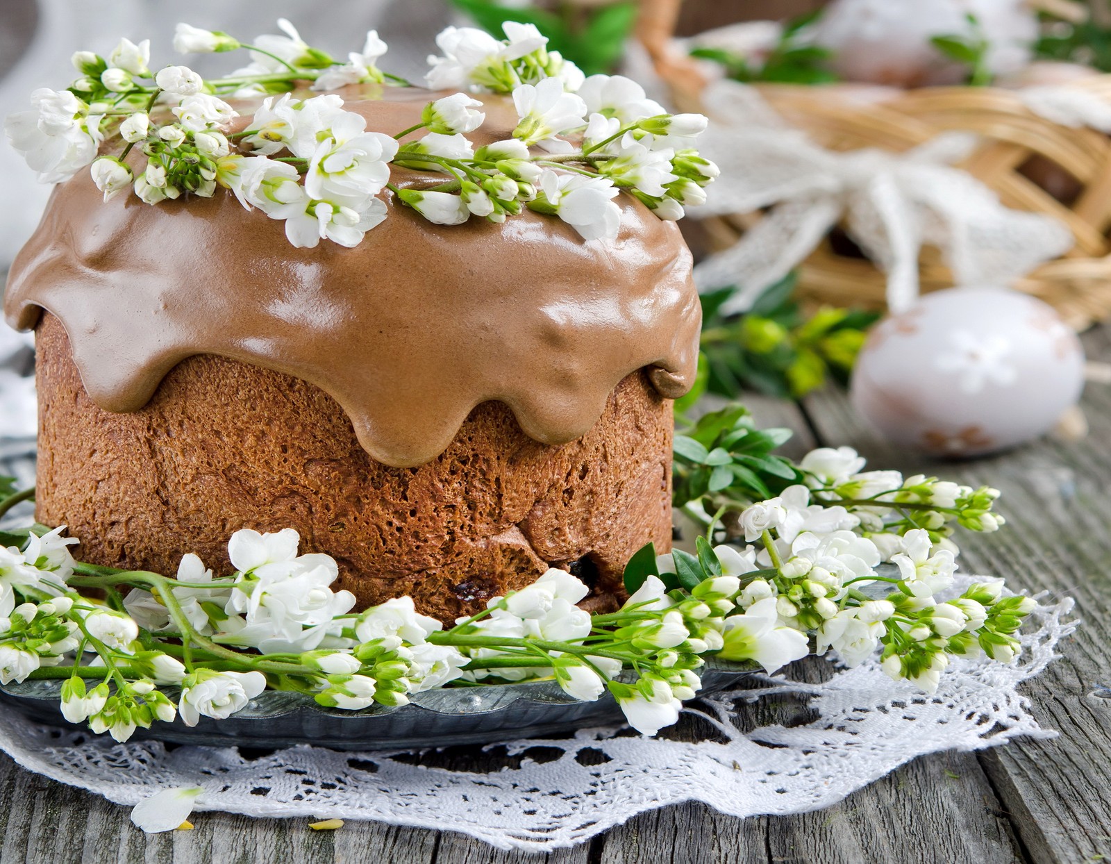 Hay un pastel con glaseado de chocolate y flores blancas en un plato (pastel de chocolate, pascua, pastel de pascua, kulich, huevo de pascua)