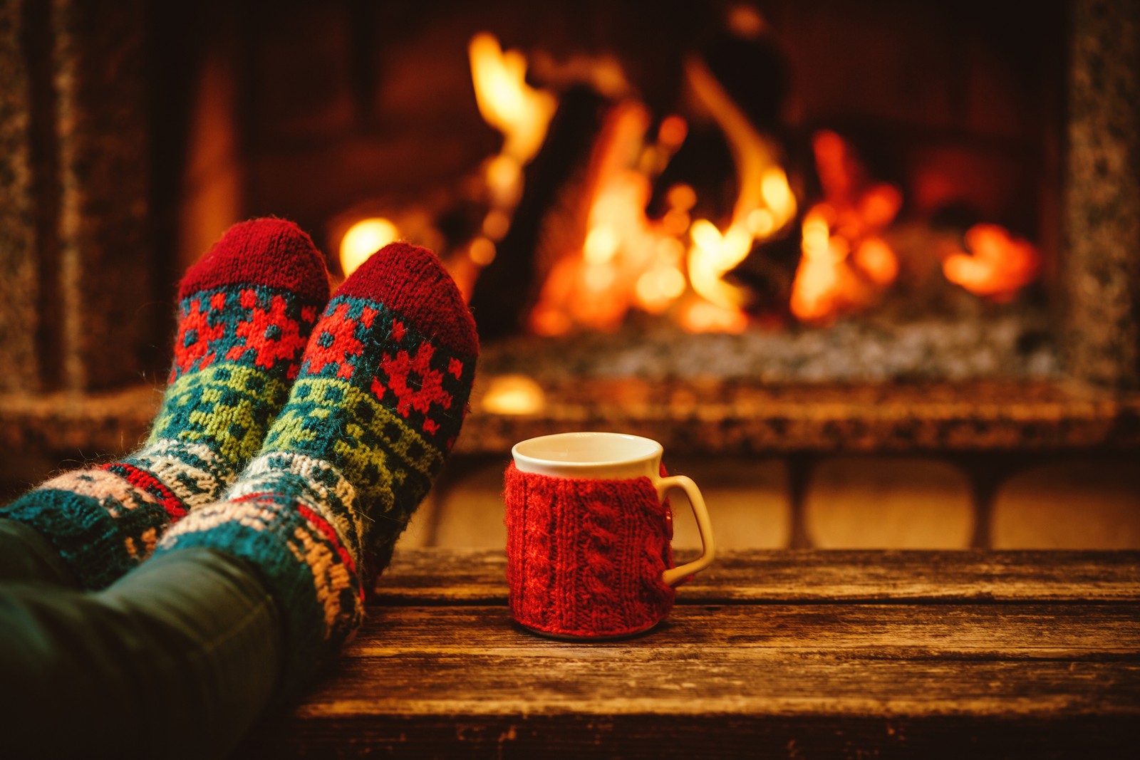 Una persona con calcetines y manoplas sentada junto a una chimenea (día de navidad, calcetín, festivo, naranja, iluminación)