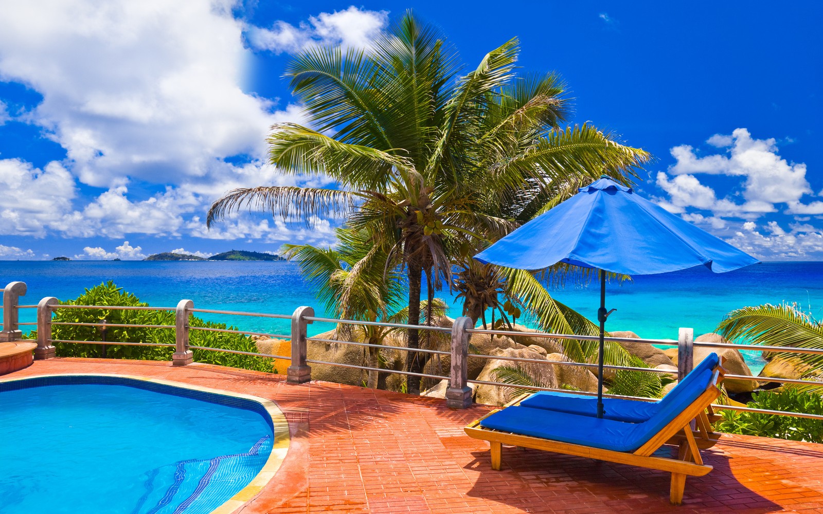 Uma vista de uma piscina e espreguiçadeiras com um guarda-sol em um deck (verão, férias, trópicos, caribenho, propriedade)