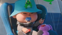 Felonius Gru Jr. with his frog hat and balloon in a car seat.