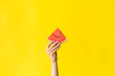 Hand Holding a Slice of Watermelon Against a Bright Yellow Background