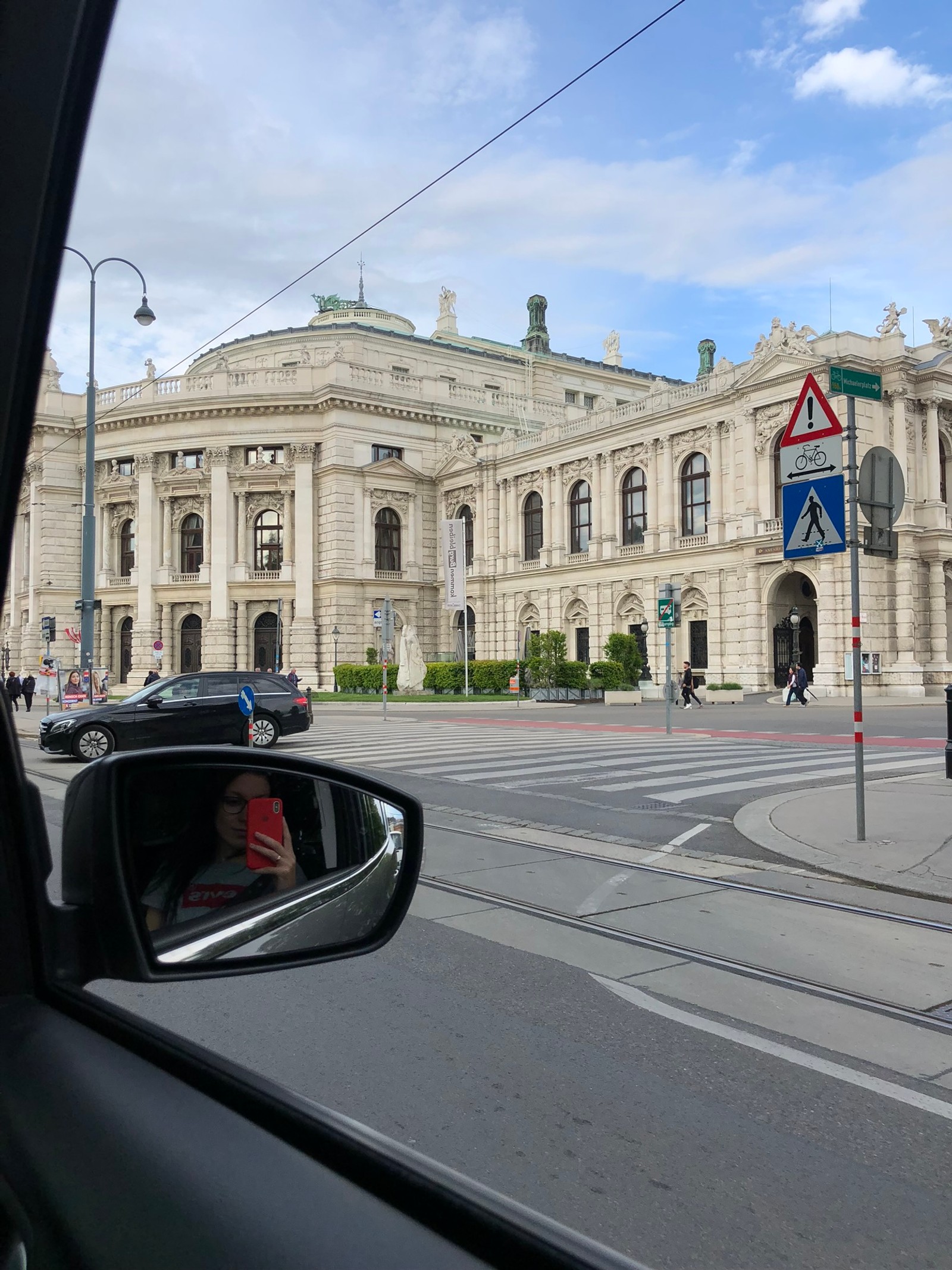 Araffe view of a car driving down a street in front of a large building (cars, automotive mirror, glass, reflection, mirror)