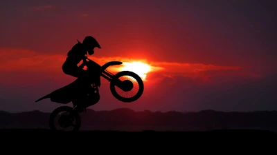 Silhueta de um performer de acrobacias de motocicleta fazendo um wheelie contra um deslumbrante fundo de pôr do sol.