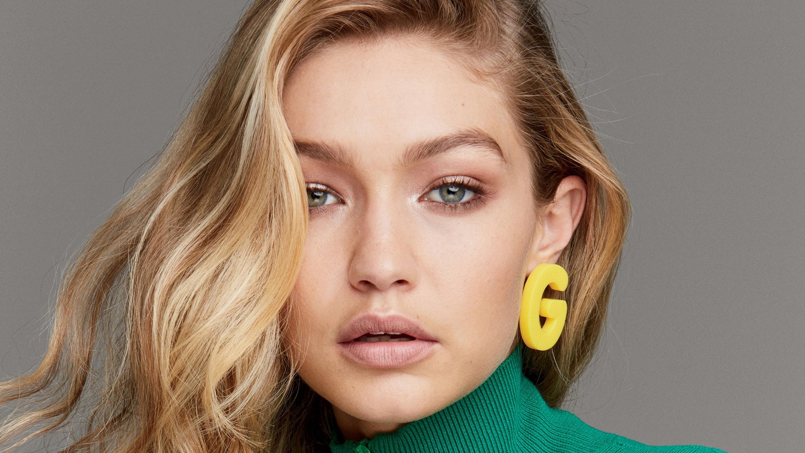 Una mujer con cabello rubio largo usando un suéter verde de cuello alto y pendientes amarillos (gigi hadid, celebridad, modelo, rubia, chicas)