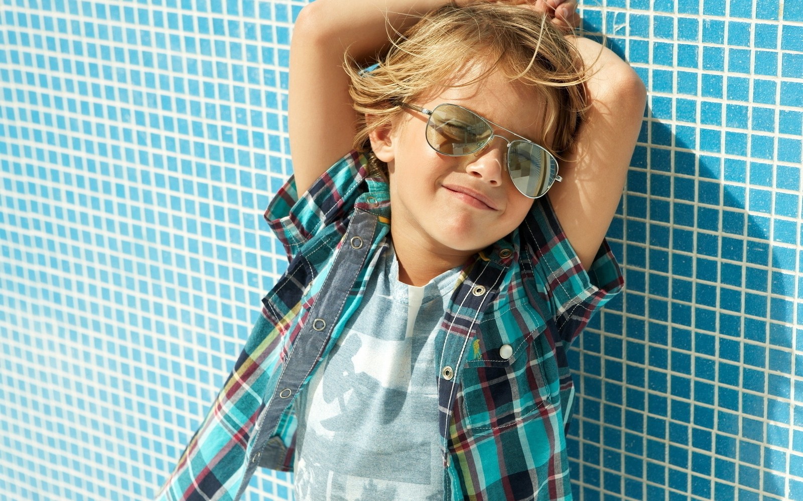 Arafed boy wearing sunglasses leaning against a blue tiled wall (hair, plaid, pattern, hairstyle, cuteness)