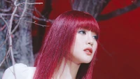 Minnie de (G)I-DLE avec des cheveux rouges frappants, posant contre un fond dramatique, incarnant l'élégance et la force.