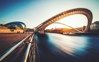 Gateshead Millennium Bridge at sunset, showcasing a striking curve over the River Tyne, with boats gliding beneath and a vibrant cityscape in the background.