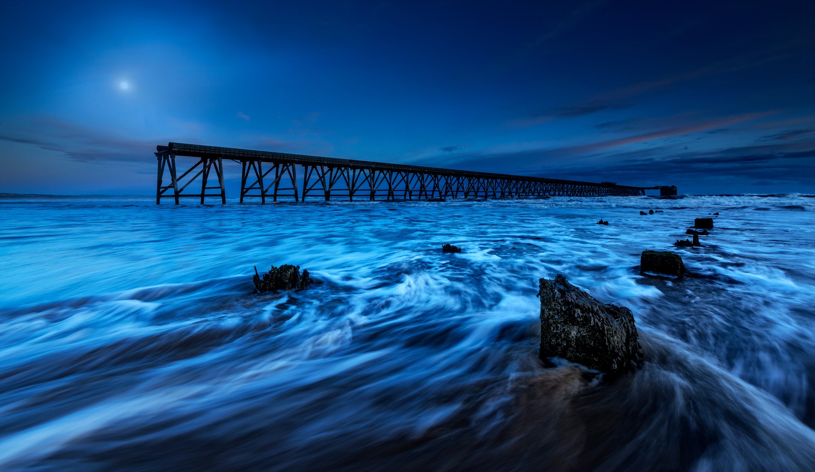 Uma foto de longa exposição de um cais à noite com ondas quebrando à sua frente (pier de madeira, luz do luar, paisagem marinha, exposição longa, cênico)