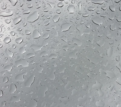 Raindrops on a windowpane, creating a textured pattern against a grey backdrop.