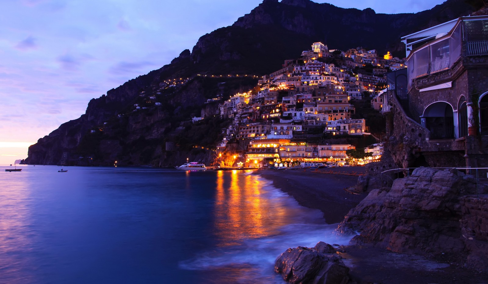 Vista aérea de uma praia com um penhasco e uma cidade ao lado (positano, mar, noite, costa, turismo)