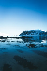 Ruhige arktische Landschaft: Blauer Gletschersee spiegelt schneebedeckte Berge unter klarem Himmel