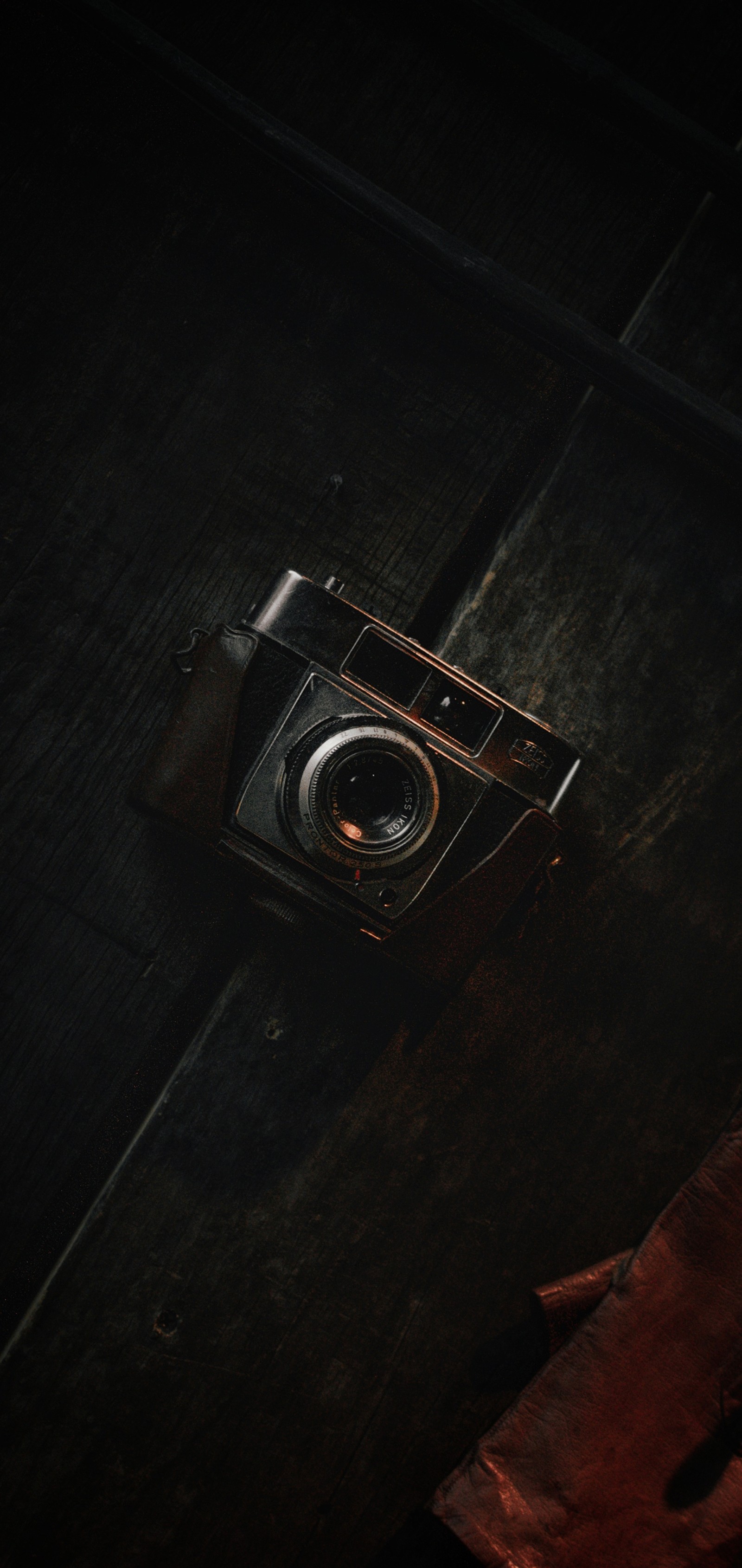 There is a camera that is sitting on a wooden table (darkness, brown, camera, camera lens, camera accessory)