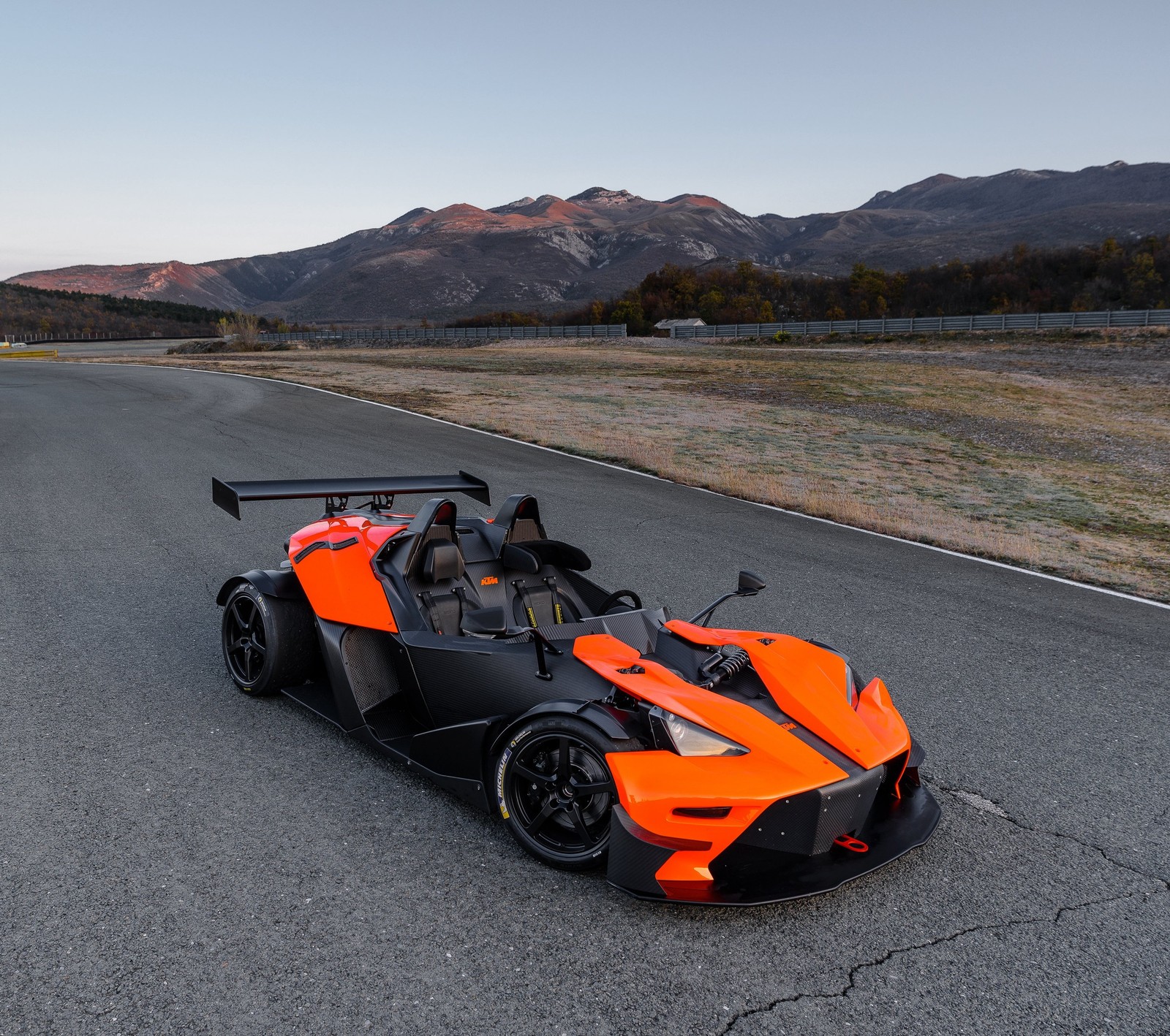 Un coche de carreras naranja y negro en una carretera con montañas de fondo (austria, negro, ktm, naranja)