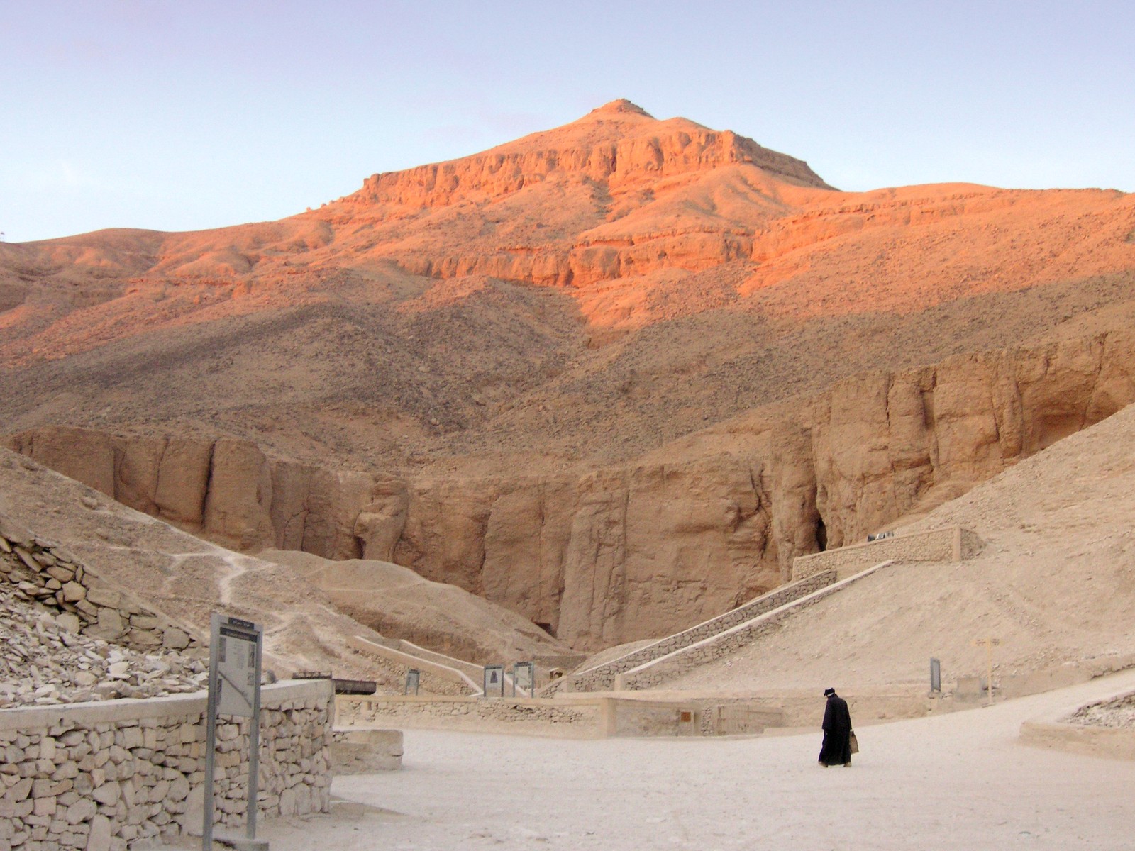 There is a person walking in the desert with a mountain in the background (ancient egypt, badlands, wadi, geology, formation)