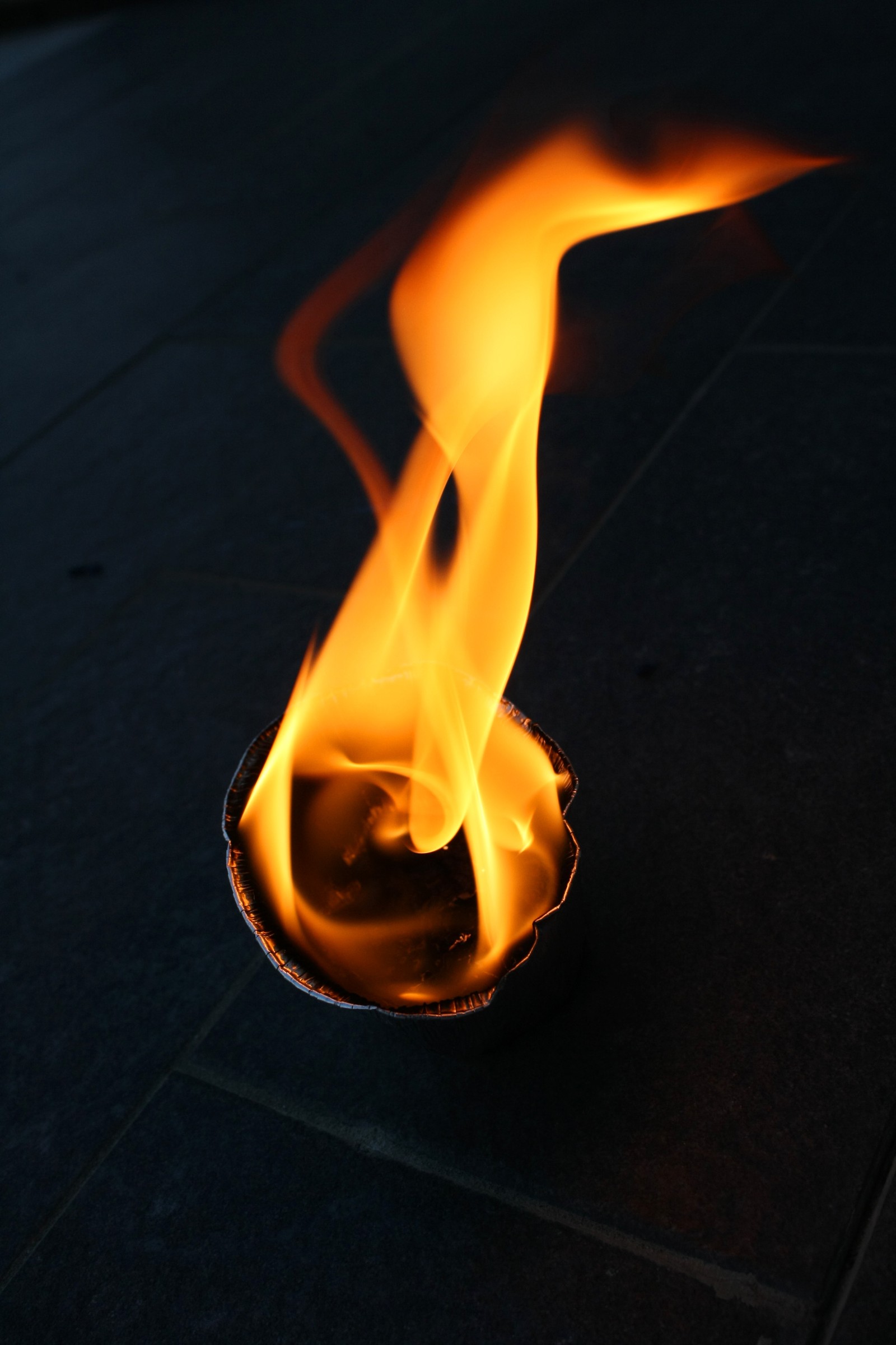 Flames are burning in a metal bowl on a sidewalk (fire, flame, heat, gas)