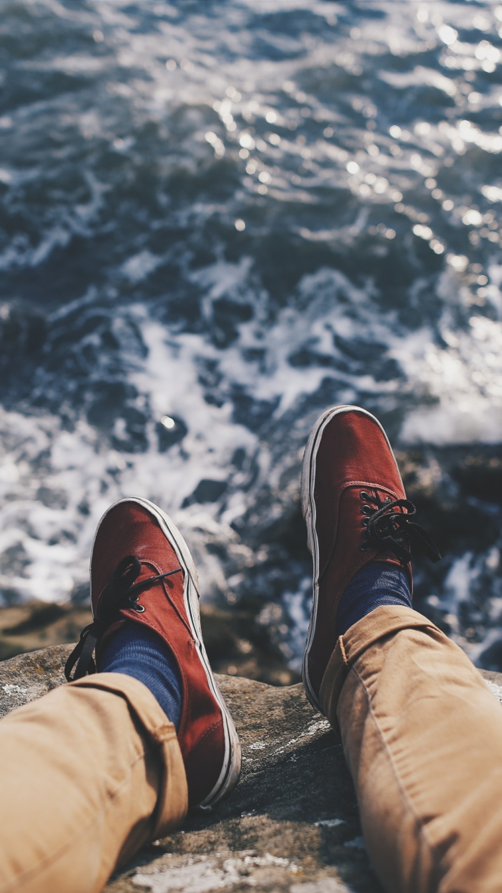 Someone is sitting on a rock by the water with their feet up (feet, sea, shoes, vacation, waves)