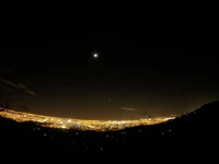 Cidade iluminada pela lua no horizonte sob um céu estrelado