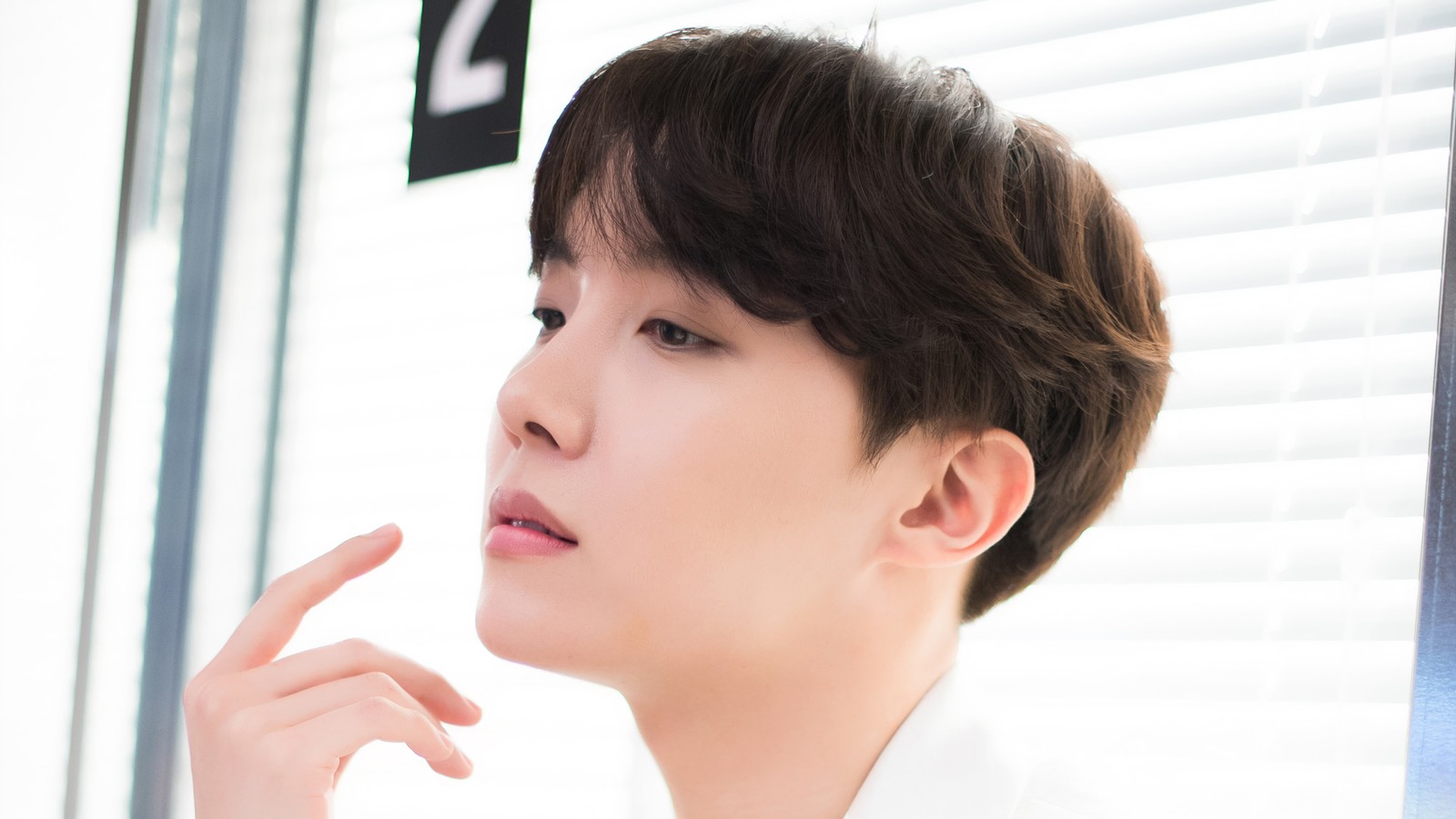 There is a man that is looking in the mirror with his hand on his chin (j hope, jung ho seok, bts, bangtan boys, kpop)