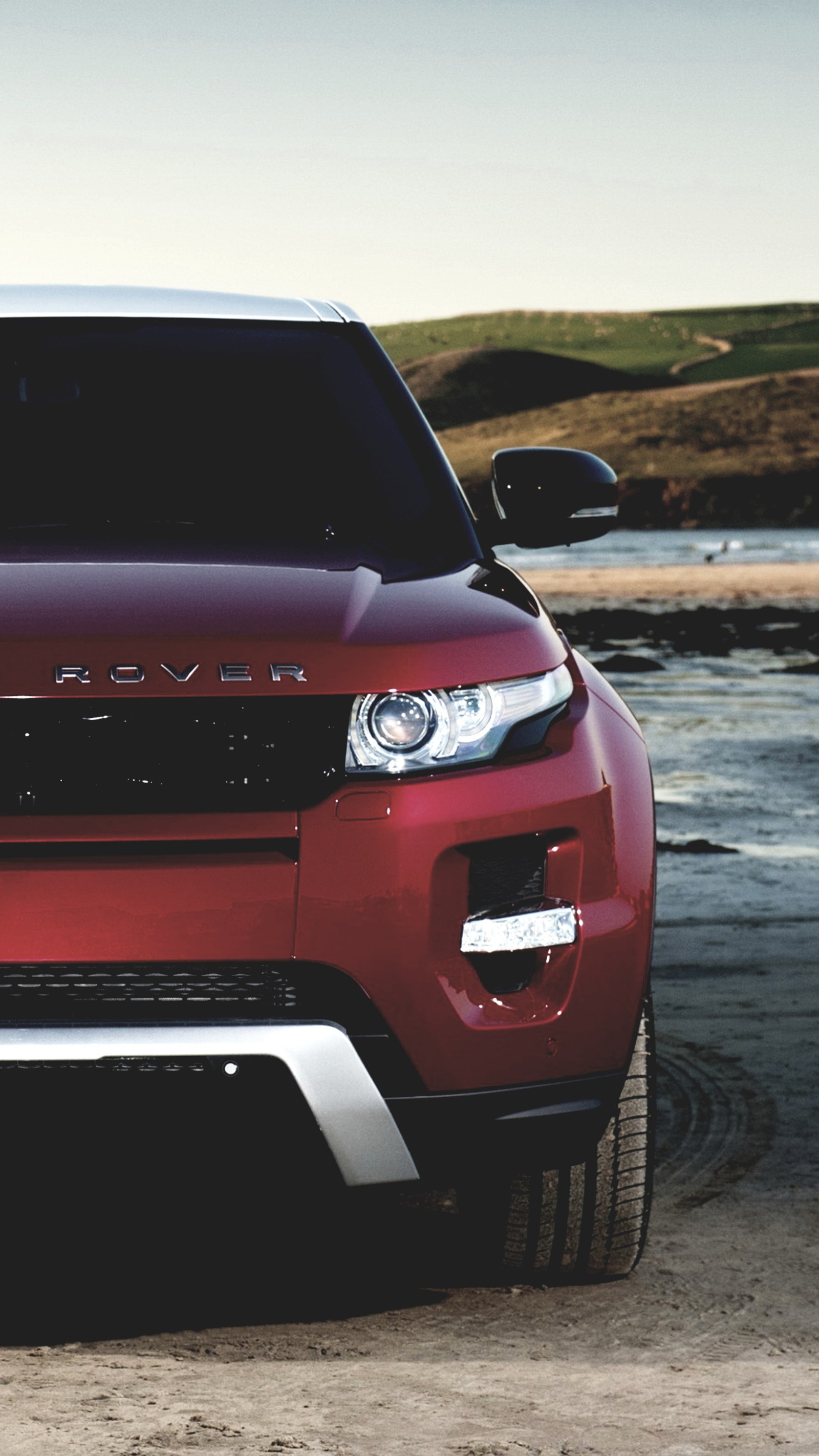 A close up of a red car parked on a beach near a body of water (car, evoque auto, range rover, range rover evoque)