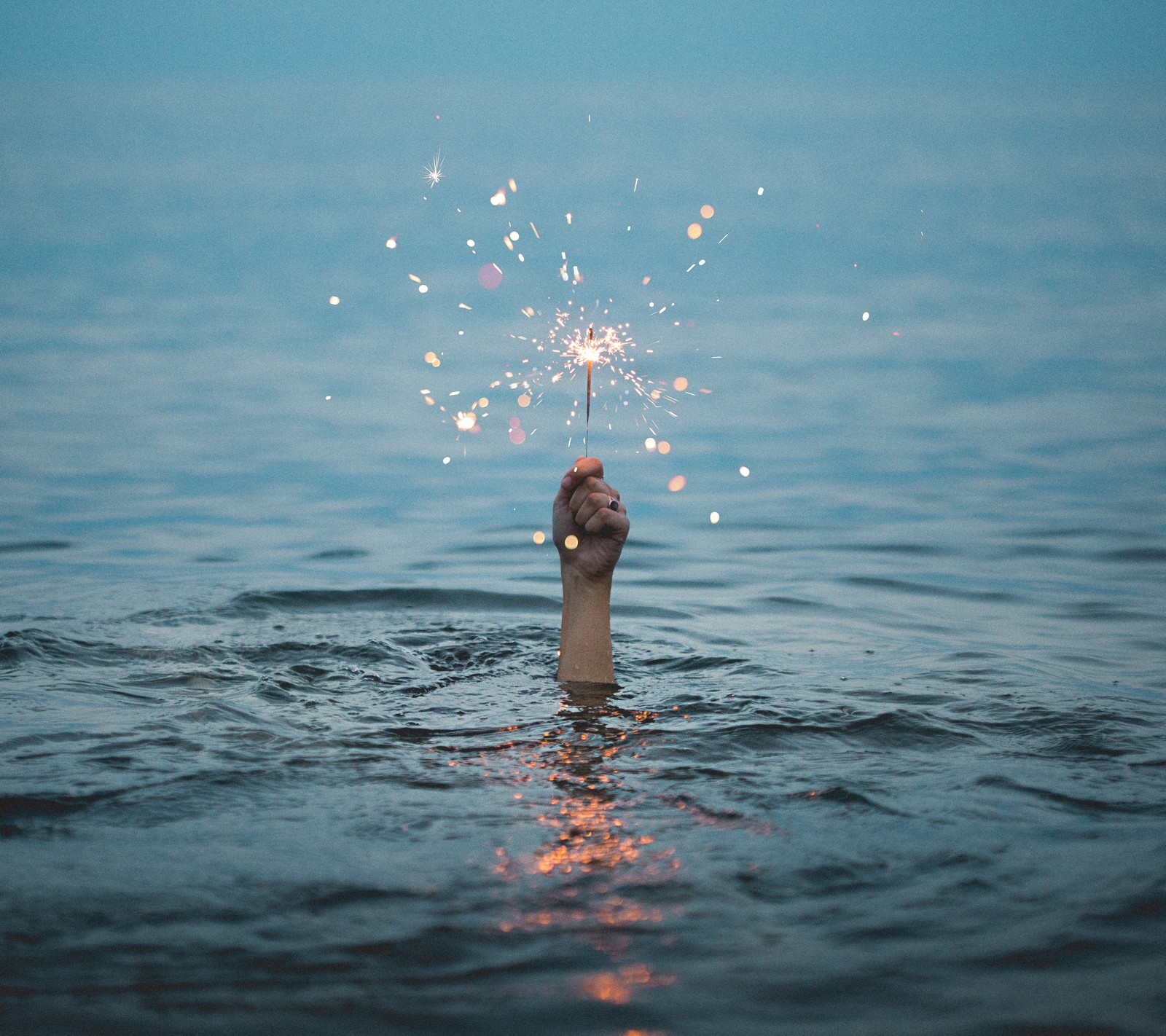 Jemand hält ein feuerwerk im wasser mit seiner hand (hand, natur, wellen, funken, wasser)