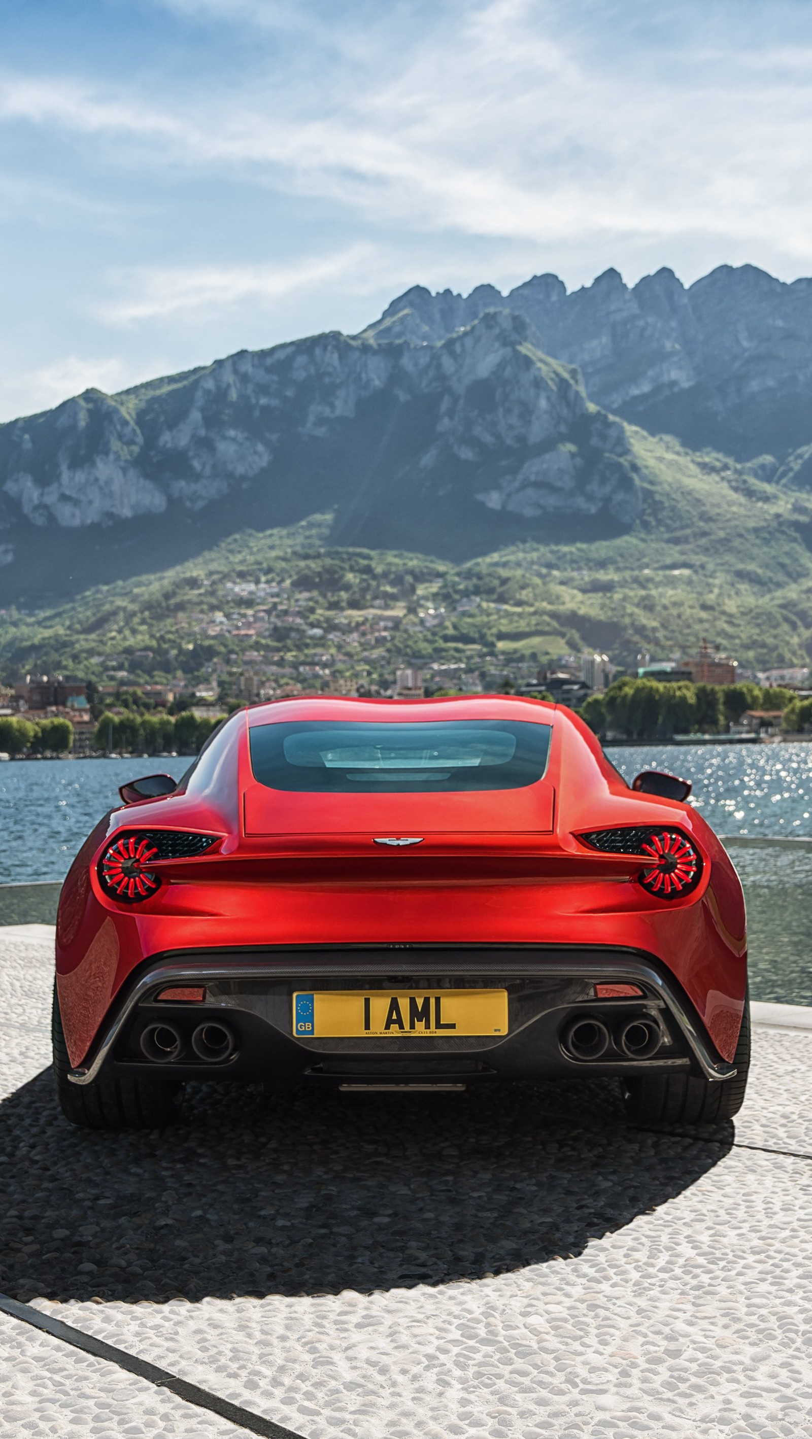 Uma vista aérea de um carro esportivo vermelho estacionado em uma estrada de pedra perto de um lago (2016, aston martin, carro, vermelho)