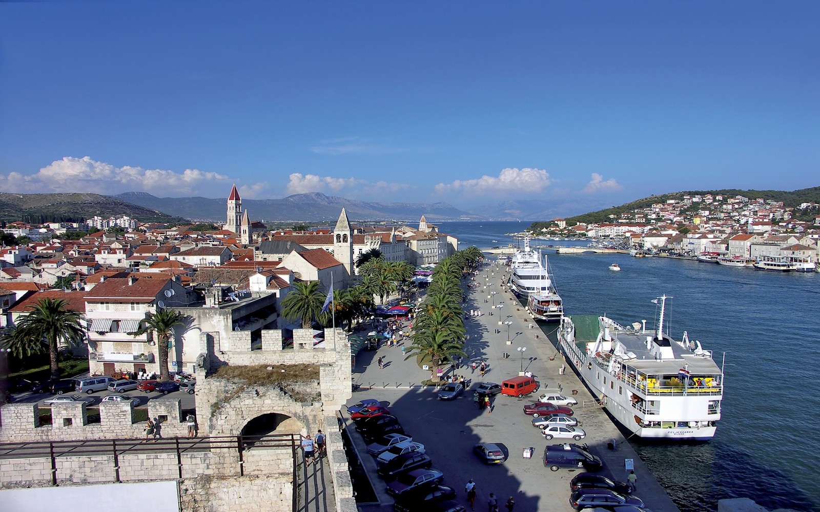 Carros estão estacionados ao lado da estrada perto da água (porto, cidade, área urbana, mar, marina)