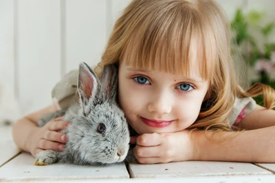 Adorables Mädchen mit blauen Augen kuschelt mit einem süßen Kaninchen