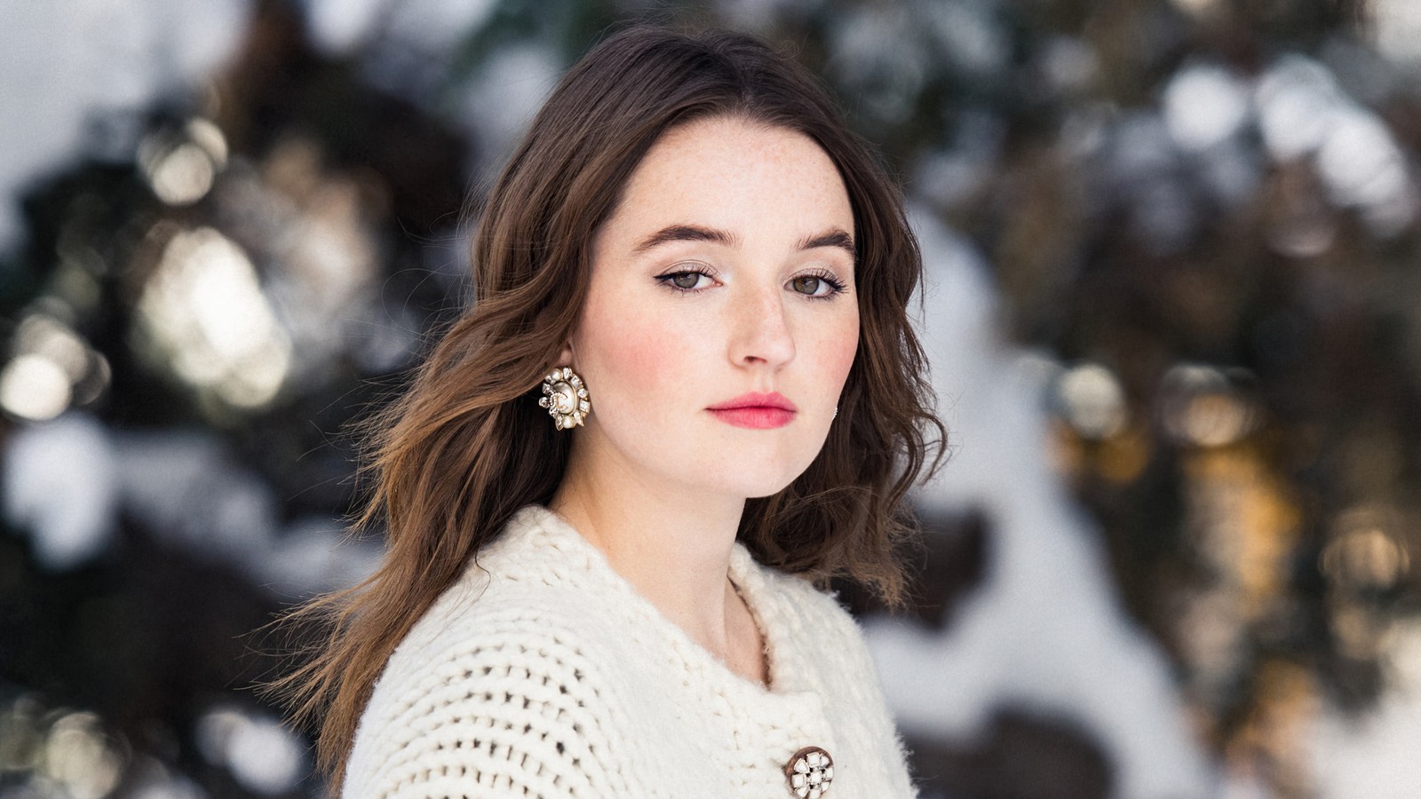 Femme en pull blanc et boucles d'oreilles se tenant devant un arbre (kaitlyn dever, actrice, célébrité, femmes, filles)