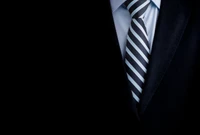 Elegant monochrome close-up of a tuxedo with a striped necktie against a dark backdrop.