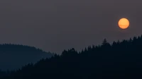 Lune de récolte se levantant au-dessus des silhouettes de montagnes à l'aube