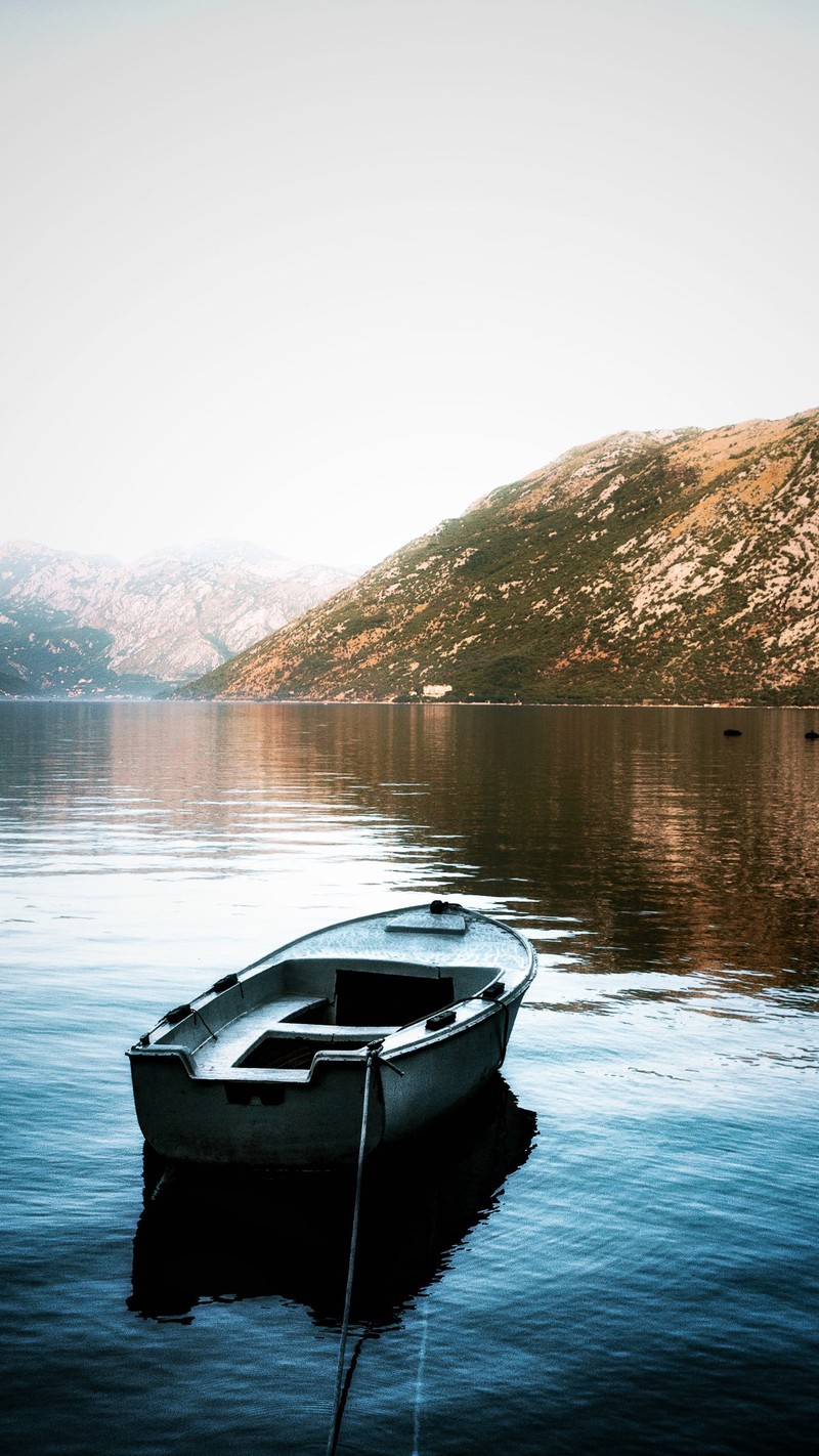 На воде привязана маленькая лодка. (отражение, вода, лодка, гора, облако)