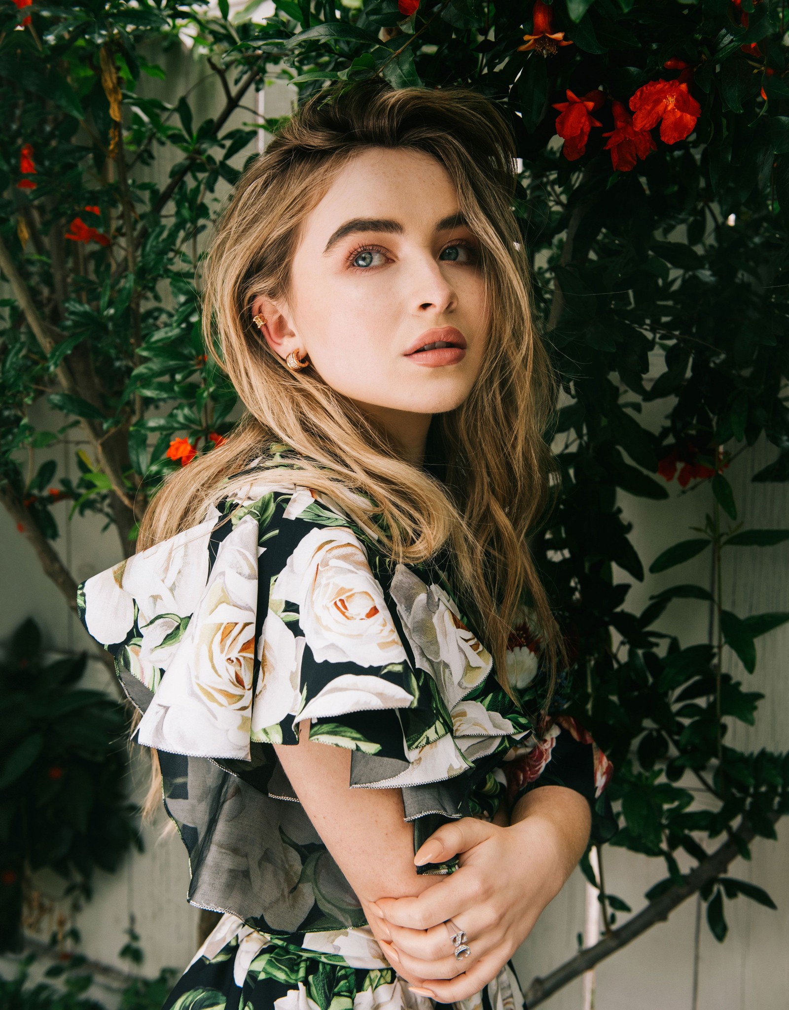 Une femme en robe fleurie se tenant devant un arbre (sabrina carpenter, chanteur américain, portrait, belle fille, gens)