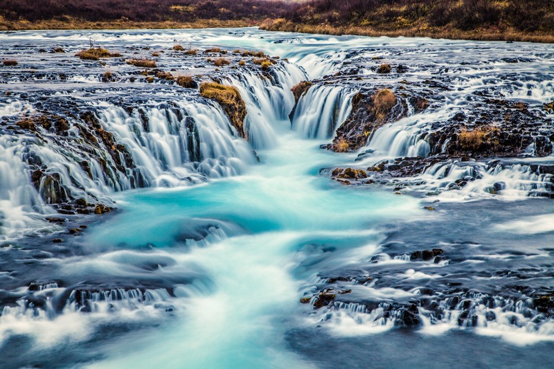 Водопад, падающий по скалам в реку в исландии (bruarfoss waterfall, исландия, река поток, голубая вода, пейзаж)