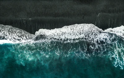 Vue aérienne des vagues océaniques turquoise s'écrasant sur la plage de sable noir