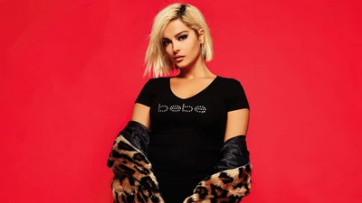 Bebe Rexha in einem schwarzen Kleid vor einem lebhaften roten Hintergrund, der Selbstbewusstsein und Stil ausstrahlt.