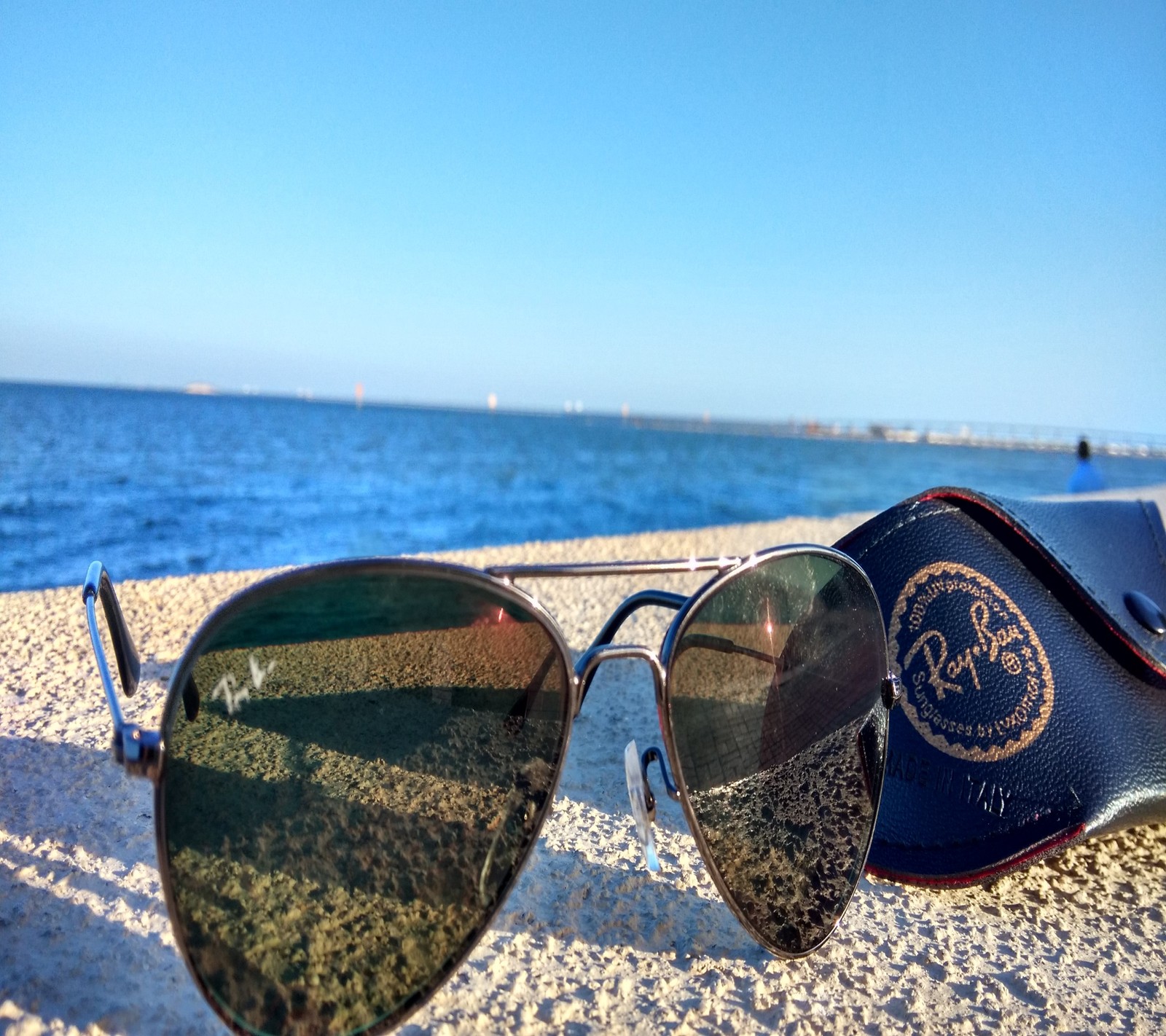 Óculos de sol com uma case na areia perto da água (óculos, rayban, mar)