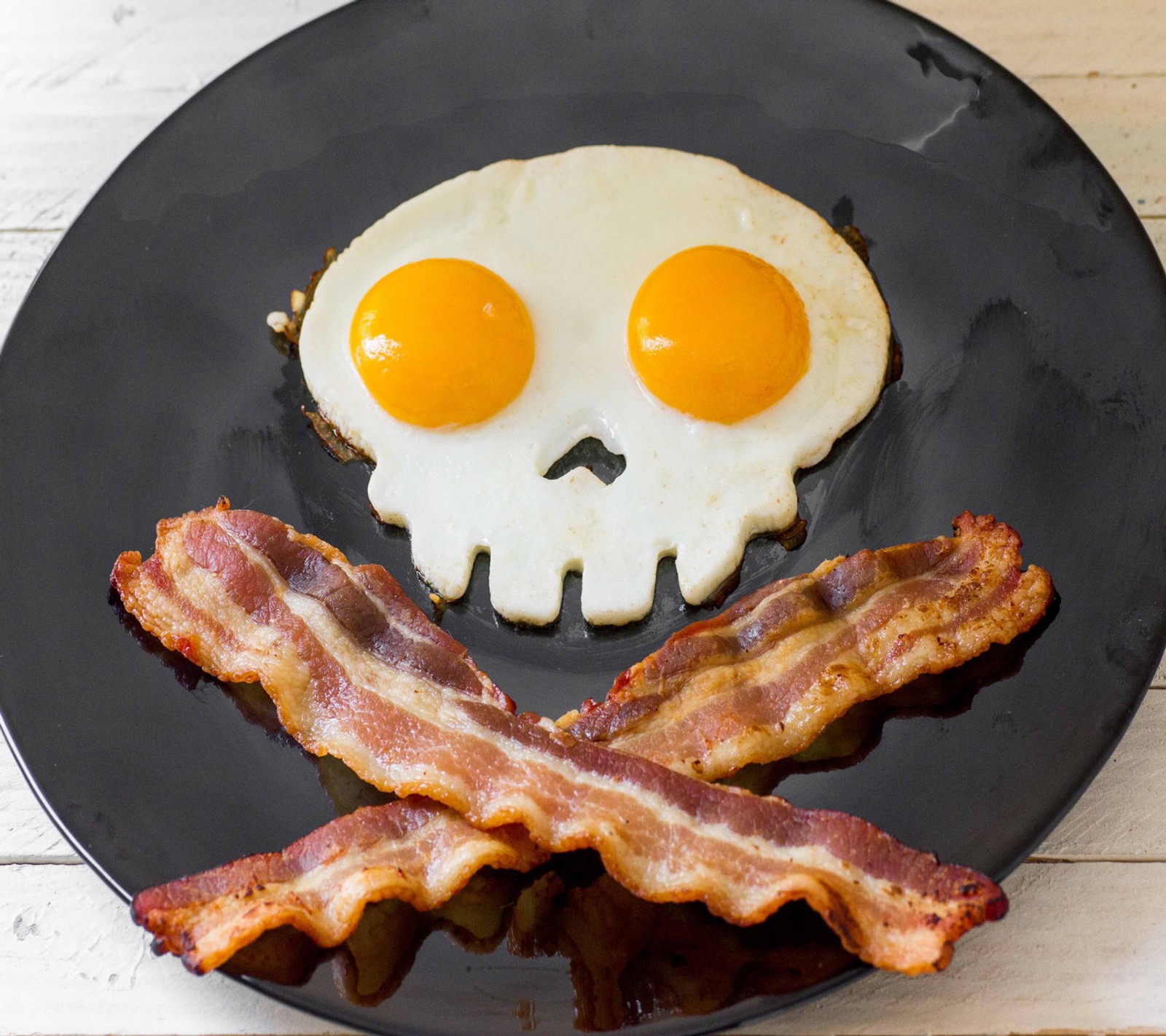 There is a plate with bacon and eggs on it with a skull (bacon, breakfast, crossbones, eggs, evil)