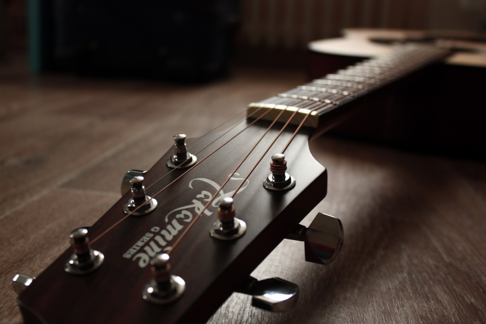 Há uma guitarra que está em uma mesa (violão, instrumento de cordas, instrumento musical, instrumentos de cordas dedilhadas, guitarra elétrica)