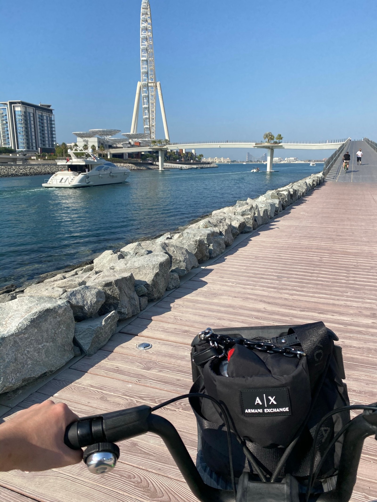 Alguém andando de bicicleta em um calçadão perto de um corpo d'água (água, acessório de bicicleta, saco, torre, embarcação)