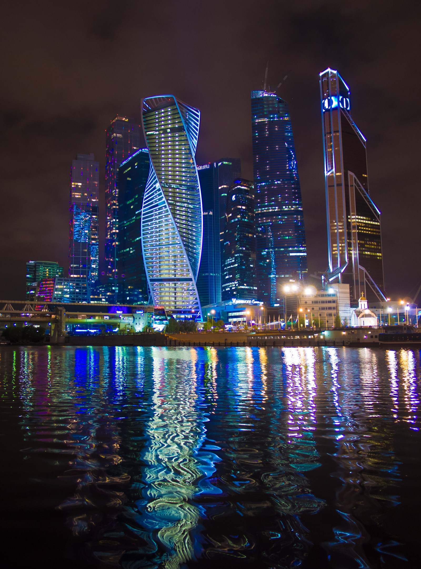 Освещенные небоскребы в городе ночью, отражающиеся в воде (небоскреб, москва, телефон, вода, здание)