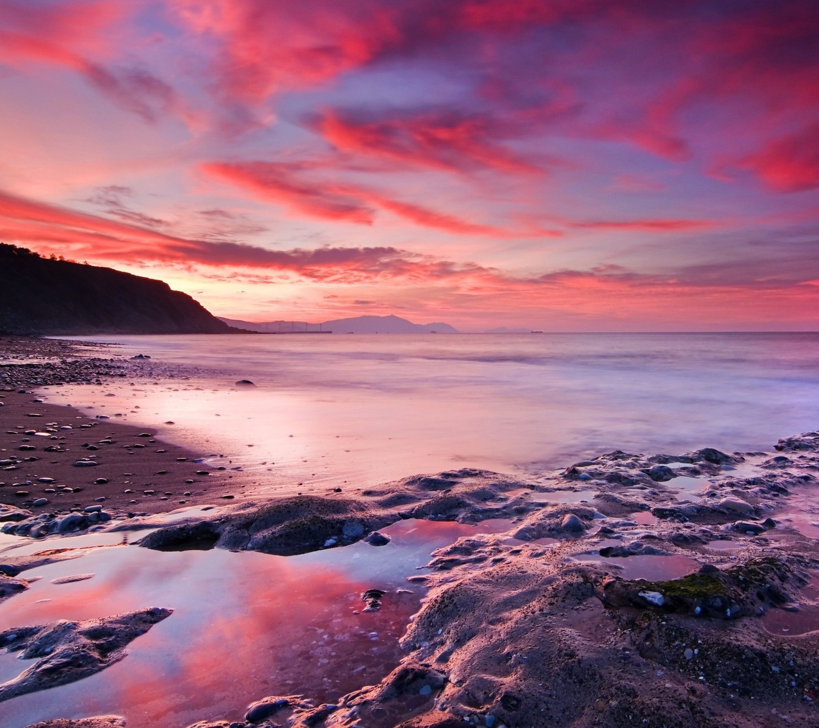 Uma vista de uma praia com pedras e água ao pôr do sol (praia, nascer do sol)