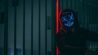 Anonymous Figure in Neon Glow Mask Against Urban Backdrop