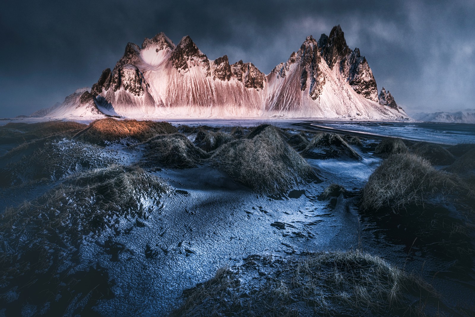 Um close-up de uma montanha com um corpo d'água em primeiro plano (vulcânico, montanha vestrahorn, islândia, praia de areia preta, stokksnes)