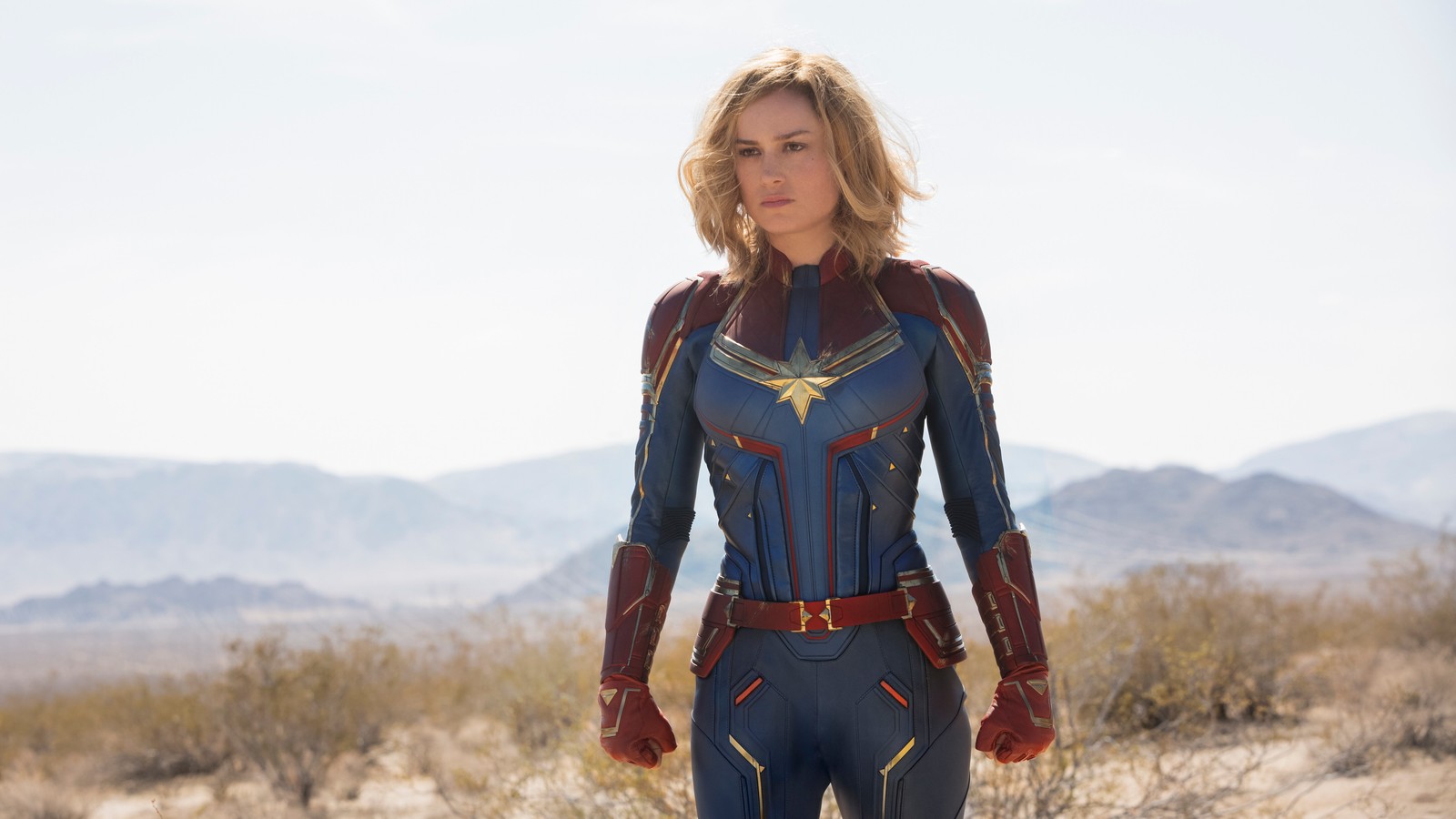 Una mujer en un traje de capitana marvel de pie en el desierto (capitana marvel, captain marvel, carol danvers, universo cinematográfico de marvel, marvel cinematic universe)