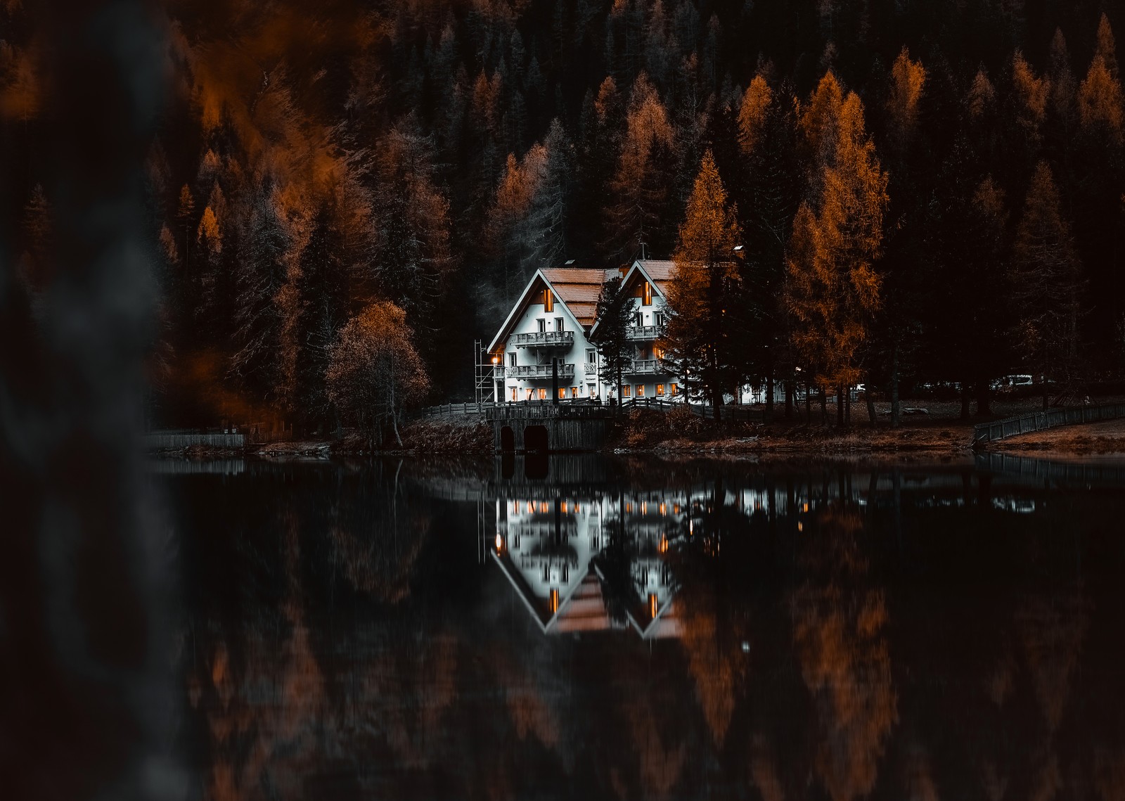 Un primer plano de una casa cerca de un cuerpo de agua (chalet, antholzer see, lake antholz, nature park rieserferner ahrn, otoño)