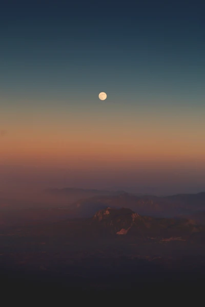 Nascer da lua sobre um horizonte sereno ao amanhecer com suaves tons iluminando o céu.