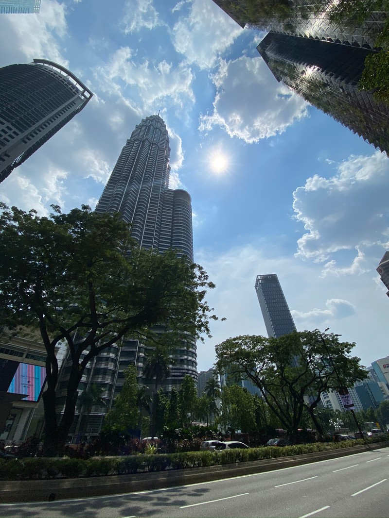 В городе много высоких зданий, и солнце светит сквозь облака (кuala lumpur, дневное время, башенный блок, архитектура, облако)