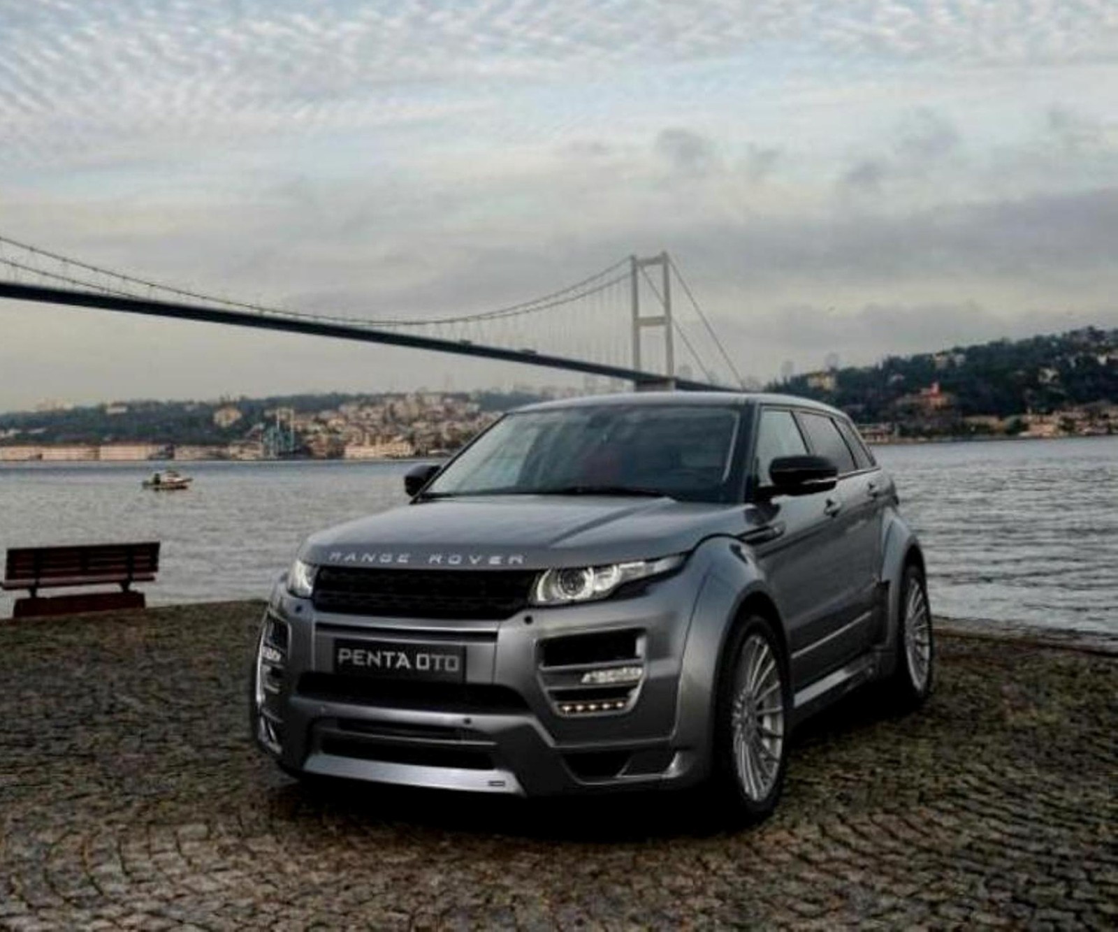 A grey range rover parked in front of a bridge near water (car, new, range, rover)